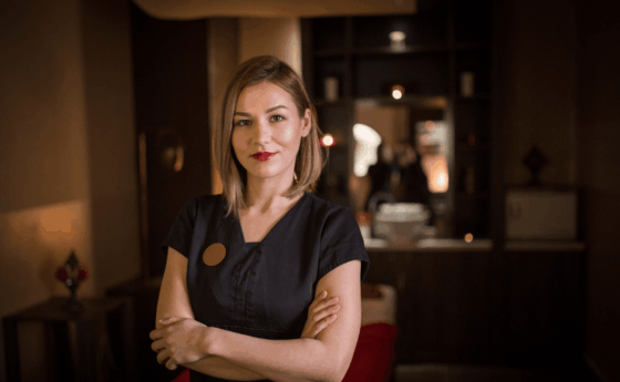 female-wellness-spa-staff-member-in-black tshirt-standing-cross-armed-in-dark-wellness-space
